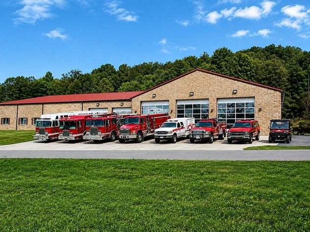Fire station with multiple red fire trucks parked in front under a clear blue sky.