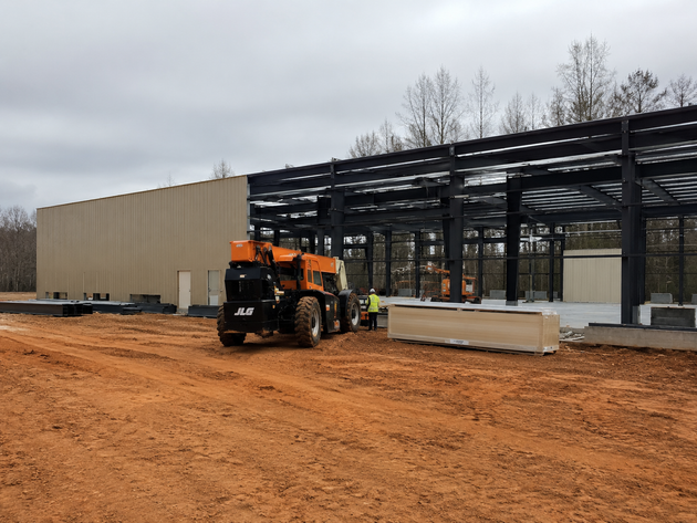 Construction site with orange loader beside a steel building frame and beige wall panels.
