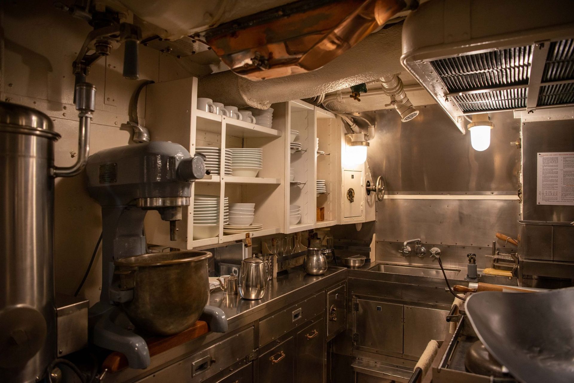 A ship galley - stainless, overhead piping and a commercial mixer