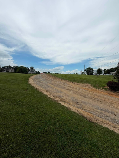 Gravel path curving through a grassy field under a cloudy sky