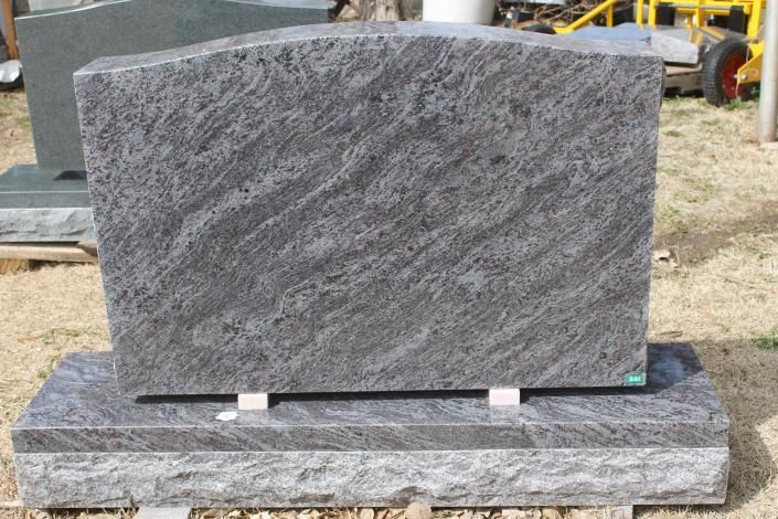 Gray granite headstone on a matching base outdoors, with a curved top and polished surface.