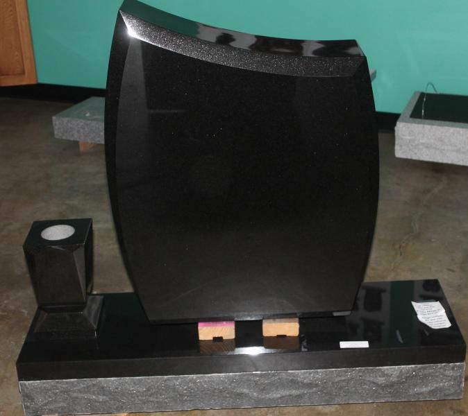 Black granite tombstone with a curved headstone and small memorial items on the base.