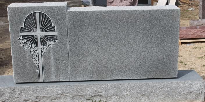 Gray granite grave marker with a carved cross and cross-shaped inset on the left side