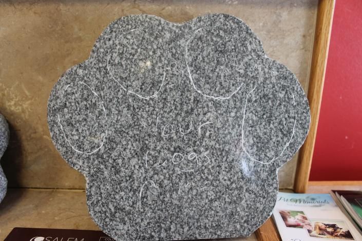 Gray flower-shaped stone plaque with white veining displayed indoors on a shelf