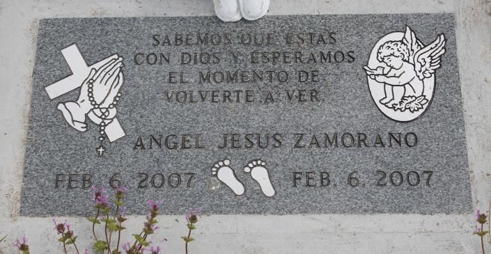 Gray memorial plaque with Spanish inscription and angel illustrations on a stone wall, dated Feb. 6, 2007.