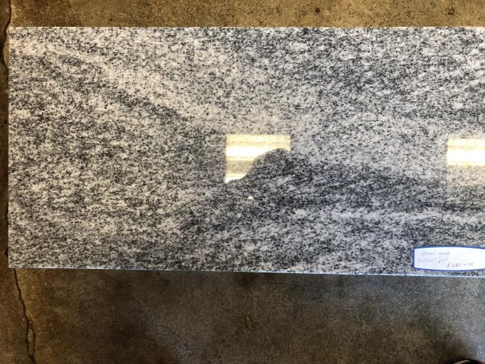 Gray speckled granite slab mounted against a brown wall, with a small white label at lower right.