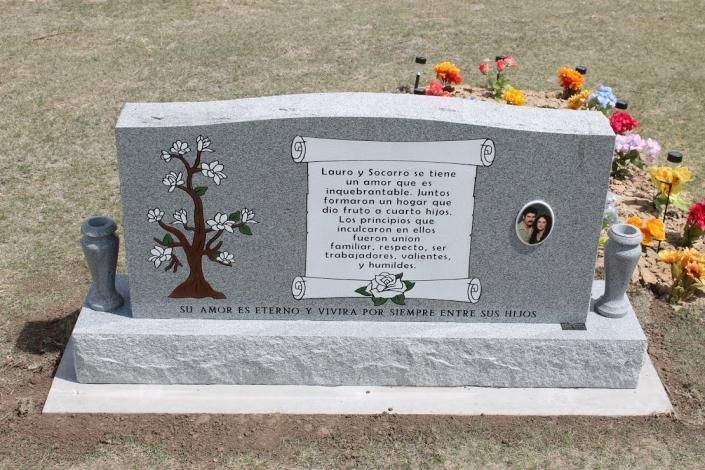 Gray memorial headstone with flowers on top and a small portrait plaque, set on a grassy cemetery plot