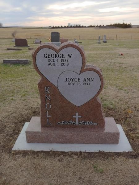 Two-heart gravestone in a cemetery field, engraved George W. and Joyce Ann, with a cross on the base.