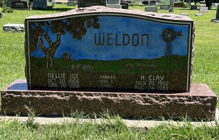 Weathered Weldon gravestone with blue sky motif in a grassy cemetery