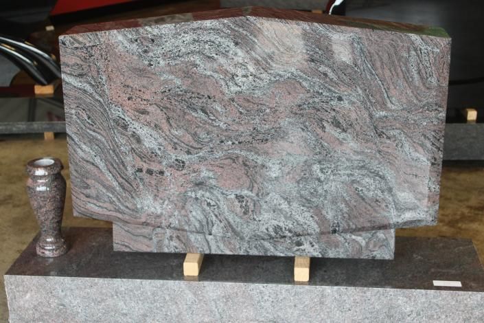 Large gray-pink stone slab displayed on a stand beside a small metallic vase indoors