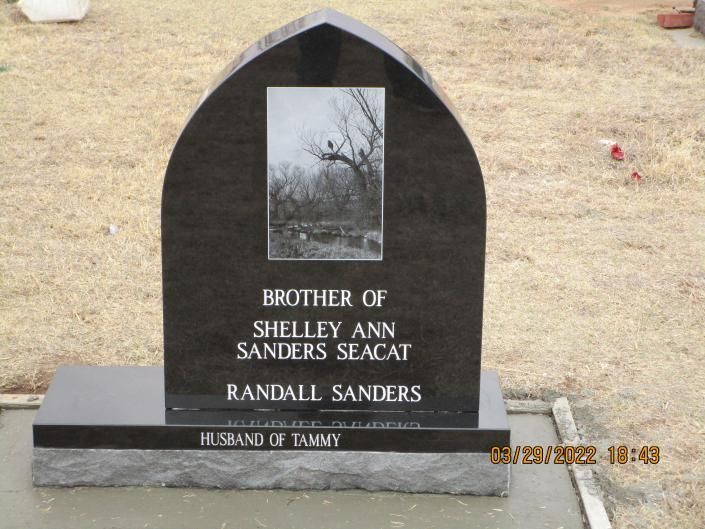 Black granite memorial headstone with engraved names and a photo plaque in a grassy cemetery area.