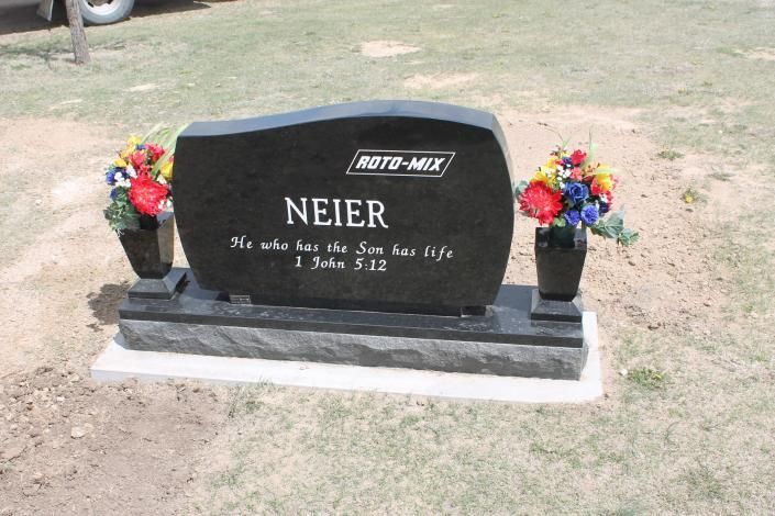 Black gravestone with flowers on both sides in a cemetery lawn.