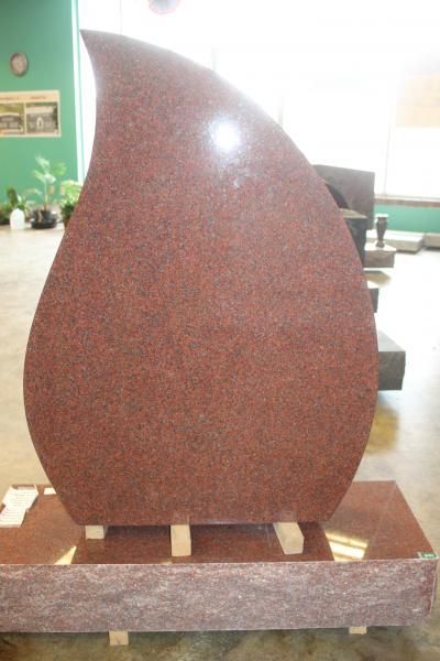 Large teardrop-shaped red stone sculpture displayed indoors on a wooden base