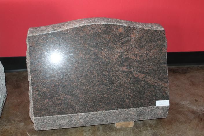 Dark granite headstone with a polished front and rough base against a red wall.