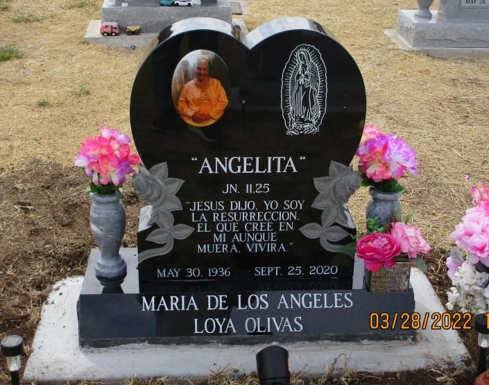 Black heart-shaped gravestone with photo, flowers, and inscription in a cemetery