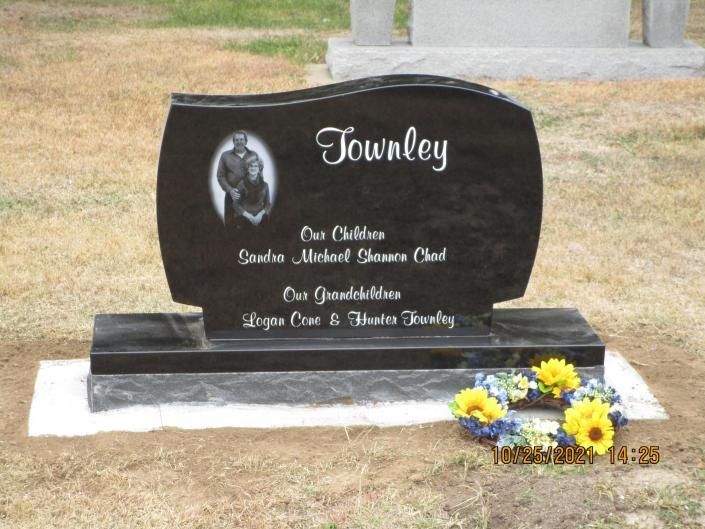 Black granite gravestone with white lettering and yellow flowers at its base in a cemetery