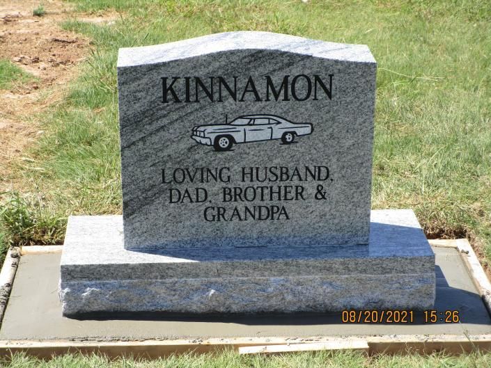 Gray gravestone engraved “KINNAMON” with car, memorializing a loving husband, dad, brother and grandpa.