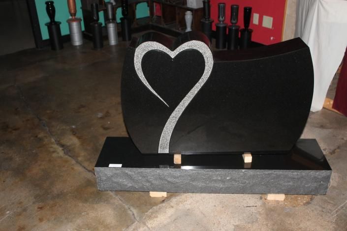 Black stone grave marker with a white heart design in an indoor setting
