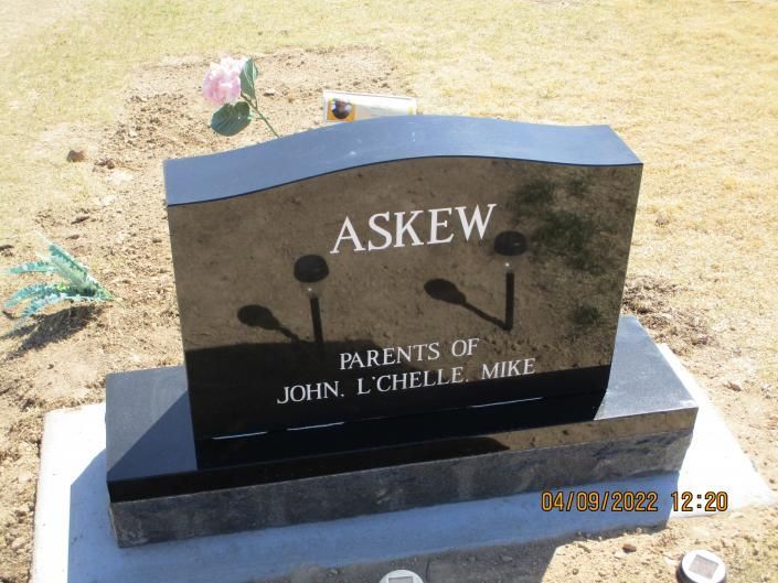 Dark gravestone with the name ASKEW and “Parents of John, Lucille, Mike” in a cemetery.