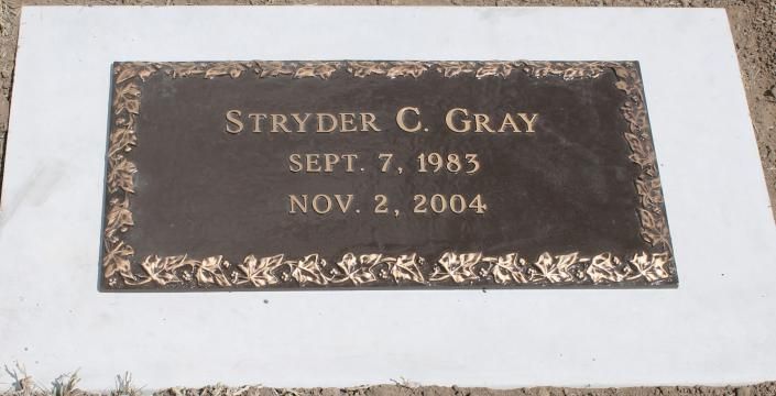 Bronze memorial plaque engraved “Stryder C. Gray” with birth and death dates on a white stone grave marker