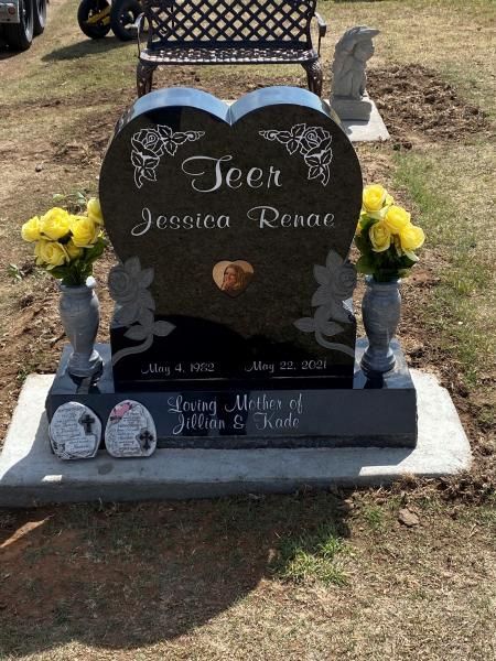 Black heart-shaped memorial headstone with flowers and small angel figurines in a cemetery