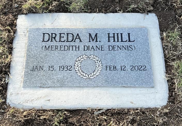 Gray granite gravestone engraved “DREDA M. HILL” with dates, lying in dry grass