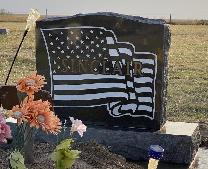 Sinclair memorial stone with American flag design in a cemetery, with flowers at the base