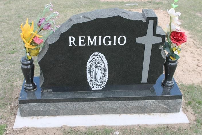Black gravestone marked “REMIGIO” with a cross, flanked by flower vases on a concrete base.