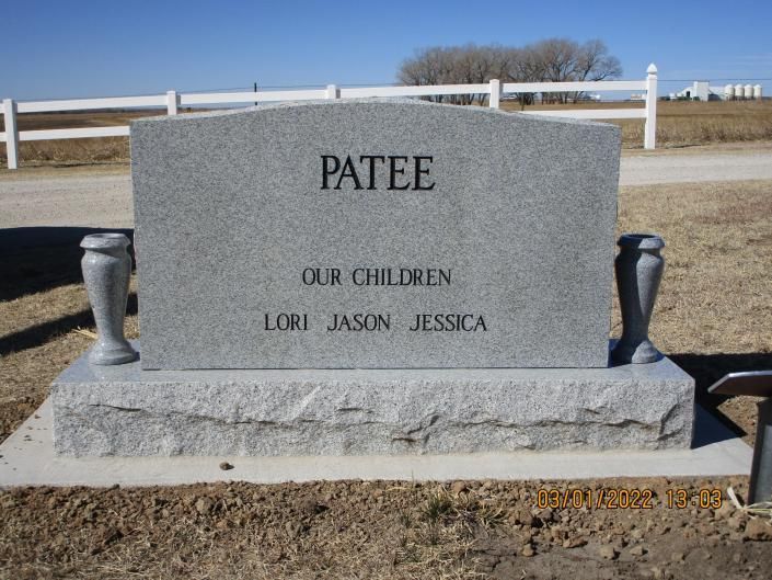 Gray gravestone engraved “PATEE” with “OUR CHILDREN” and names, set in a rural cemetery