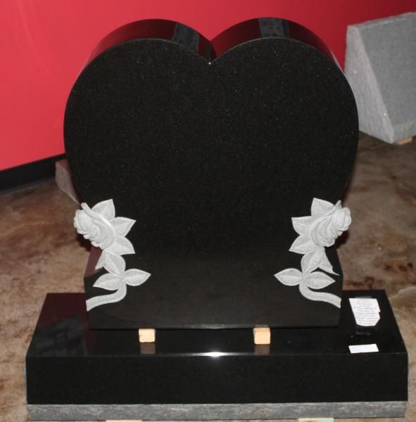 Black heart-shaped memorial headstone with white floral accents on a base