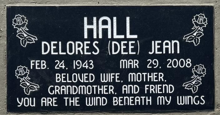 Black memorial plaque with white text and roses for Delores Dee Jean Hall, 1943–2008, “You are the wind beneath my wings.”