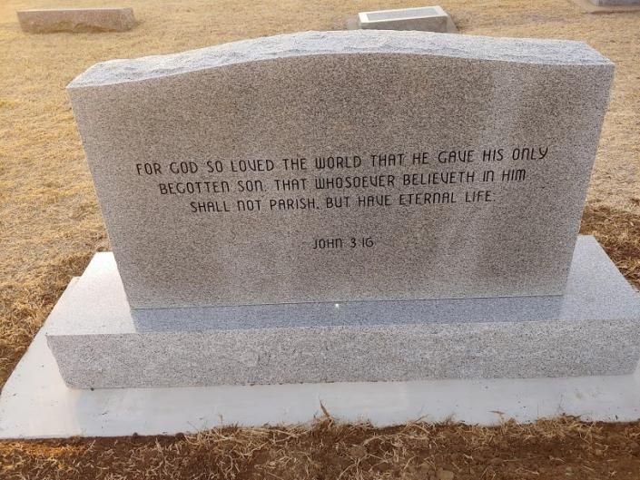 Gray granite gravestone on a white base in a sandy cemetery, with an engraved inscription.