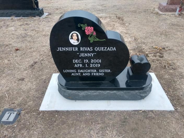 Heart-shaped black gravestone with a floral photo plaque and red flowers on a white base.