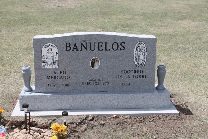 Granite memorial grave marker reading “BAÑUELOS,” with flowers at the base in a cemetery.