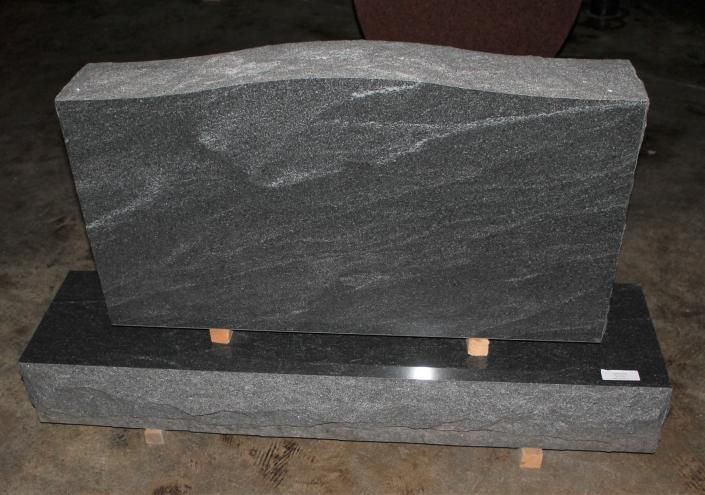 Two dark gray stone memorial slabs, one upright on a base and one lying flat behind it.