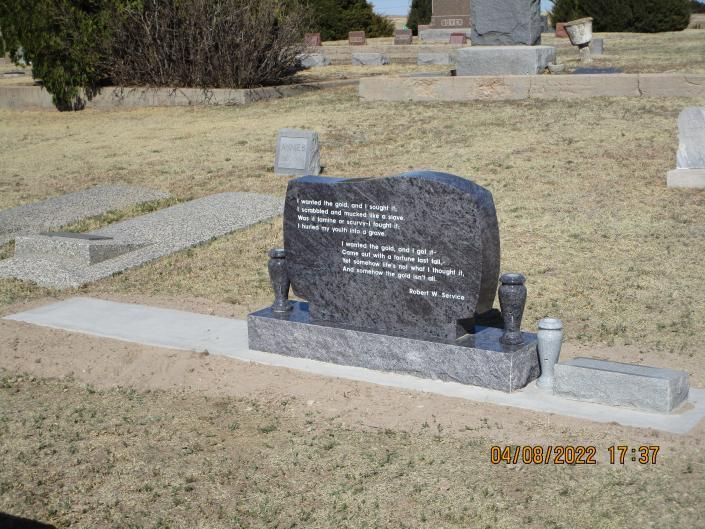 Granite gravestone with white lettering in a grassy cemetery, with small memorial items beside it