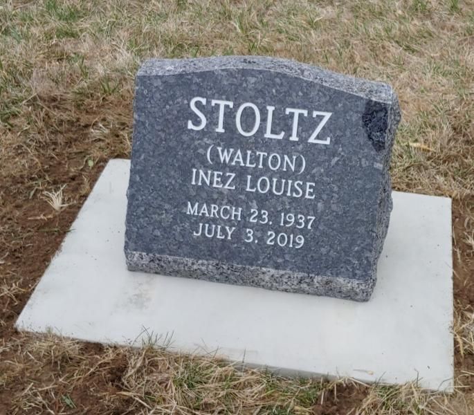 Gray gravestone on a white base in dry grass, engraved “STOLTZ” with names and dates.