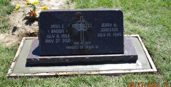 Black granite gravestone with etched cross, set in a white-bordered memorial plot on grass.