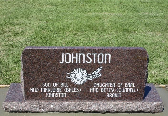 Brown memorial headstone reading “JOHNSTON” in a grassy cemetery, with engraved sunflower emblem.