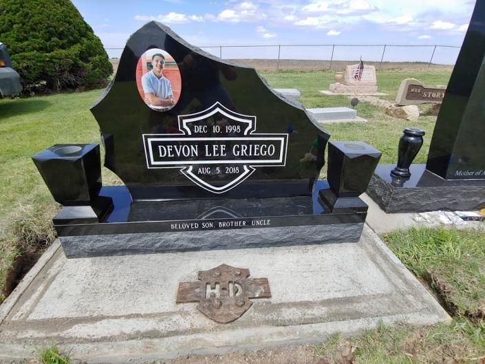 Black polished gravestone with oval portrait in a cemetery, set on a concrete base with flowers nearby.
