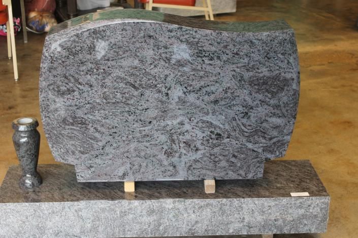Gray granite gravestone on a stone base, with a small metal vase beside it on the left.