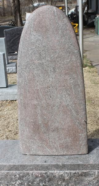 Tall pink granite headstone on a stone base outdoors