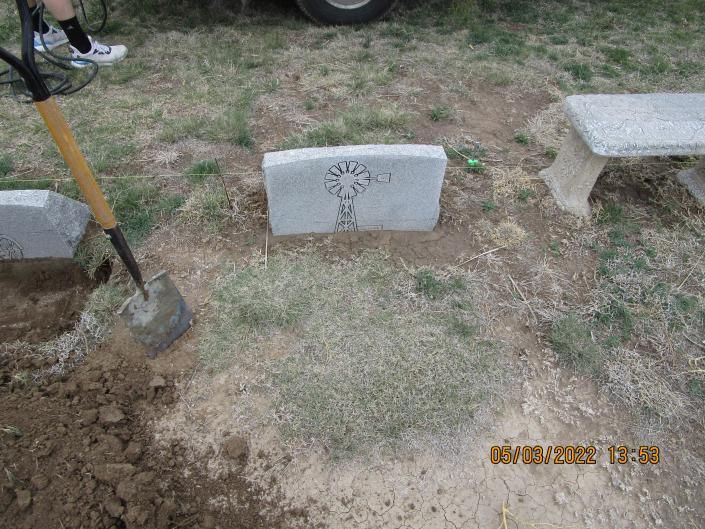 Gravestone marker in a grassy cemetery plot with a shovel nearby