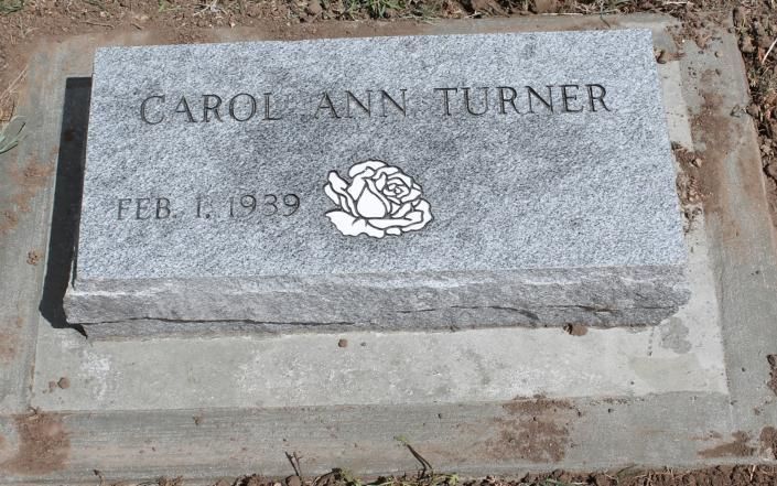Gray granite gravestone engraved “CAROL ANN TURNER” with a rose and birth date.