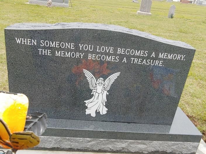 Gravestone with angel engraving and memorial quote in a cemetery, with flowers at left