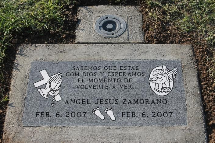 Gravestone plaque with Spanish quote and small angel and footprints, set in grass.