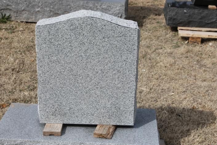 Gray granite tombstone standing on wooden supports in an outdoor yard