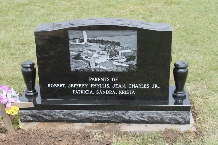Black granite memorial headstone with photo plaque and engraved names in a grassy cemetery.