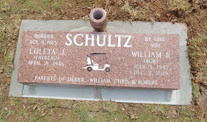 Weathered gray SCHULTZ memorial plaque with small tractor graphic in grass and dirt.
