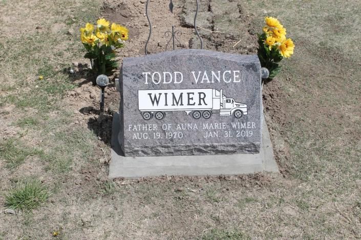 Gravestone for Todd Vance Wimer with yellow flowers on both sides in a cemetery.